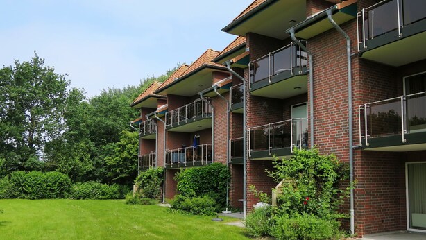 Un edificio residencial de varios pisos con fachada de ladrillo, balcones con barandillas de metal y un césped bien cuidado.