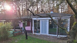 Una casa con puerta de vidrio, un pequeño porche y un jardín con banco y plantas en macetas.