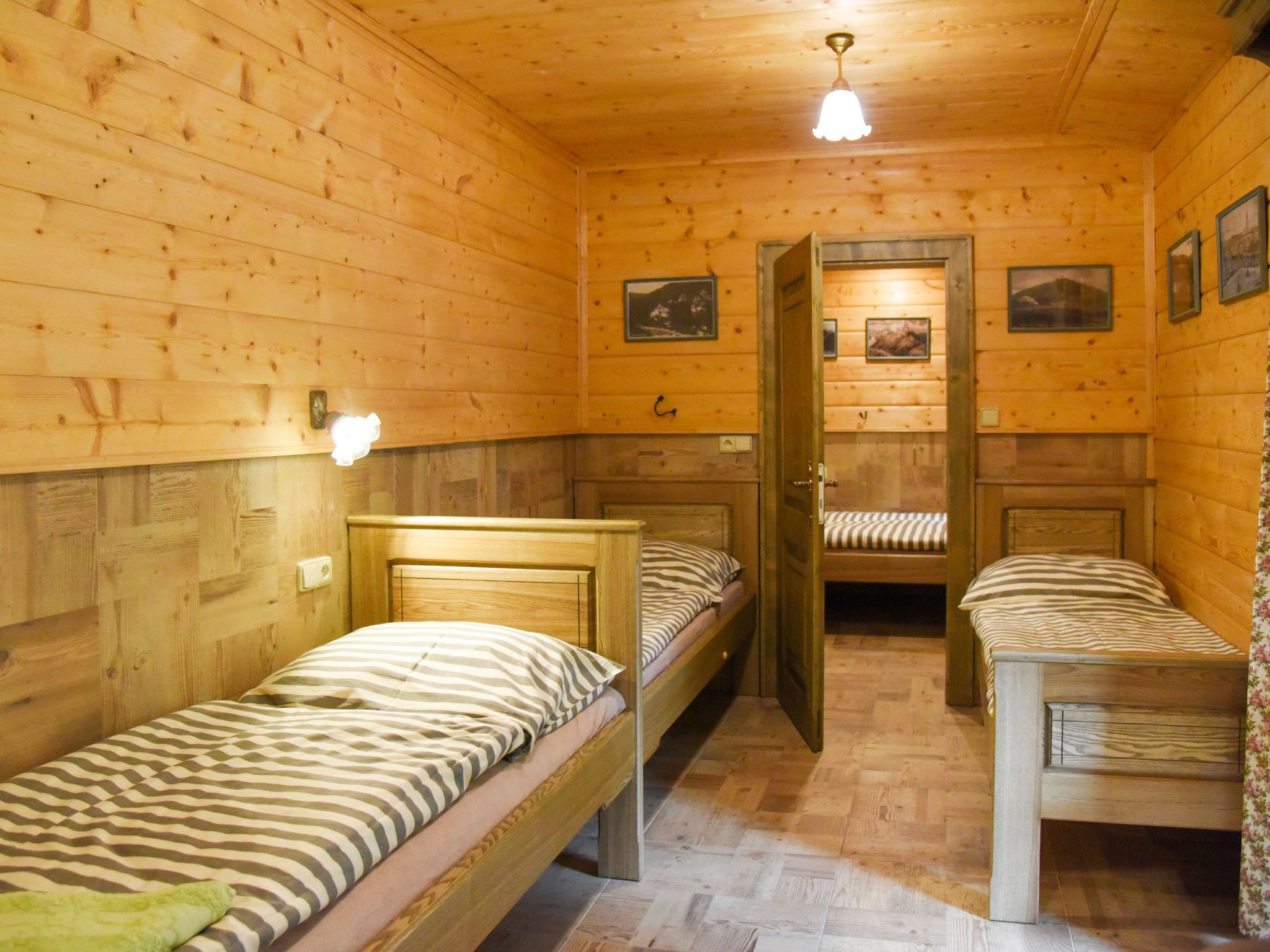 Ein Holzhüttenraum mit zwei Einzelbetten, einer Holzbalkendecke und einer Tür zu einem weiteren Raum.
