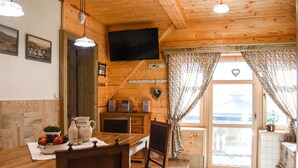 Interior acollidor d'una cabana de fusta, amb zona de dinar, cuina i un balcó amb cortines.