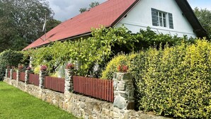 Un edificio blanco con techo rojo, rodeado de muros de piedra y diversas plantas.