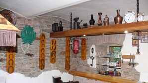 Una zona de bar rústica con estantes de madera que muestran varias botellas y vasos, una pared de piedra y una chimenea de ladrillo.