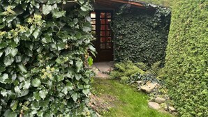 Un jardín con una estructura de madera, una tubería de metal y un sendero de piedra.
