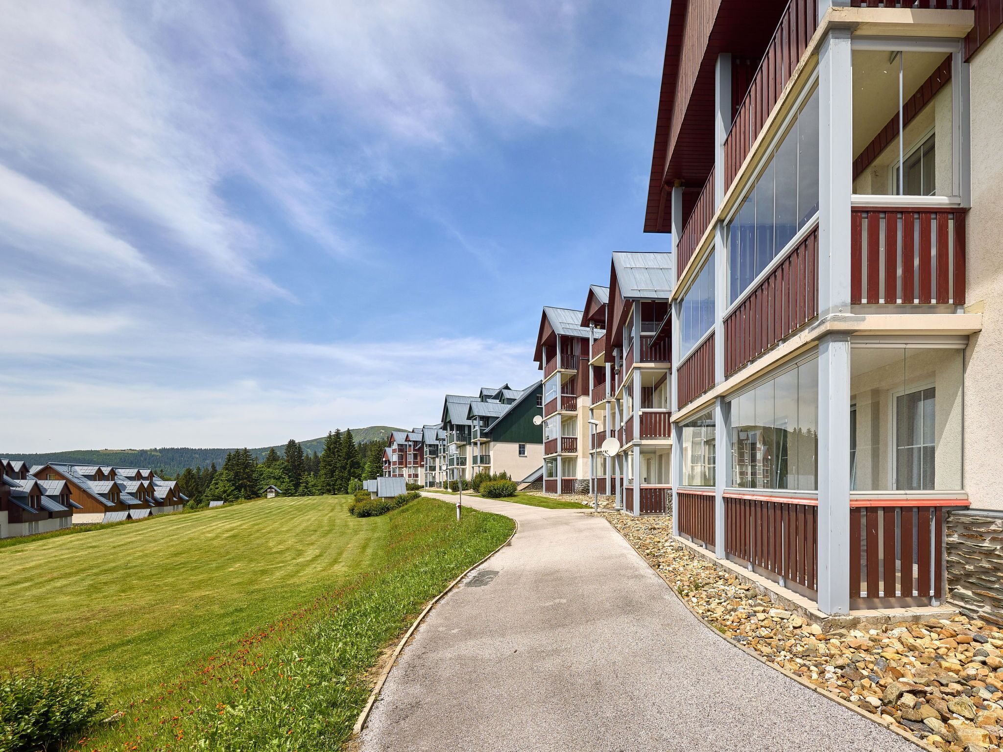A row of modern multi-story buildings with balconies, a well-maintained lawn, and a clear sky.