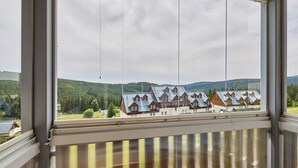 Uitzicht door een raam op een gebouw, met op de achtergrond een rij huizen, omgeven door groen en heuvels.
