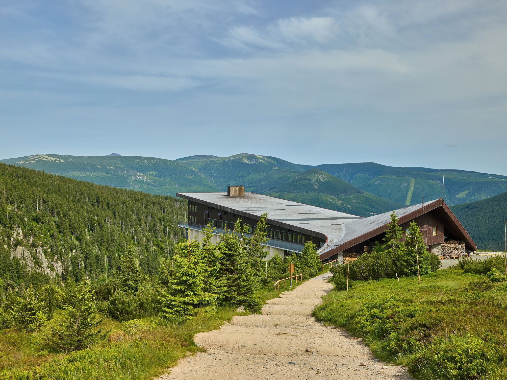 A modern building with a sloped roof, surrounded by a forested mountain landscape.