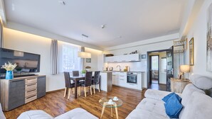 Een moderne woonkamer met een bank, een salontafel en een televisie. Er is een keuken met kasten en een eettafel.