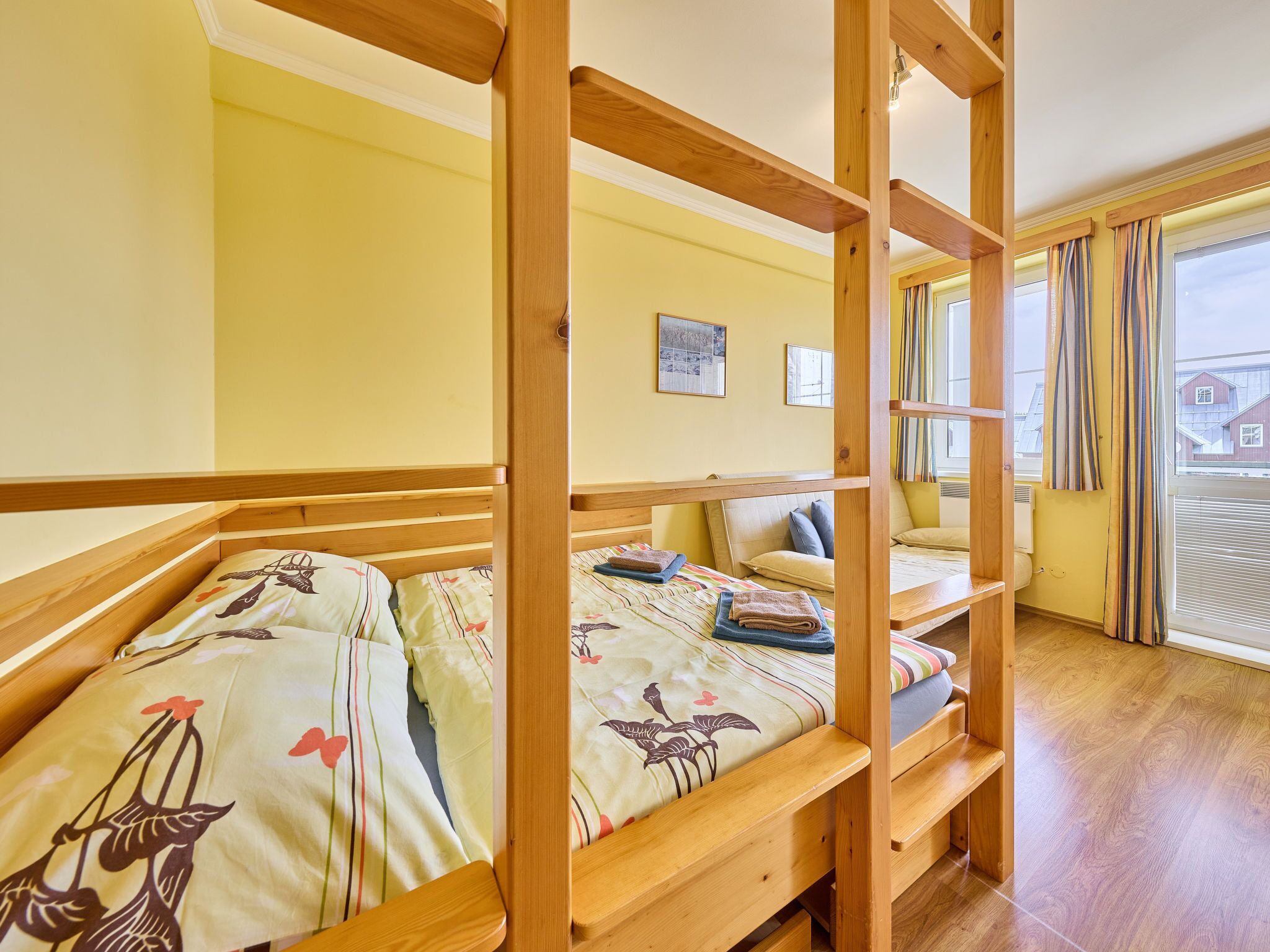 A room with bunk beds, a window with curtains, and a bed with a floral bedspread.