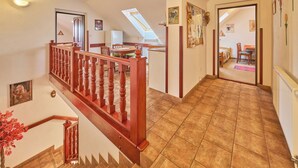 Een ruime hal met een houten trap, een eetgedeelte en een slaapkamer die door een open deur zichtbaar is.
