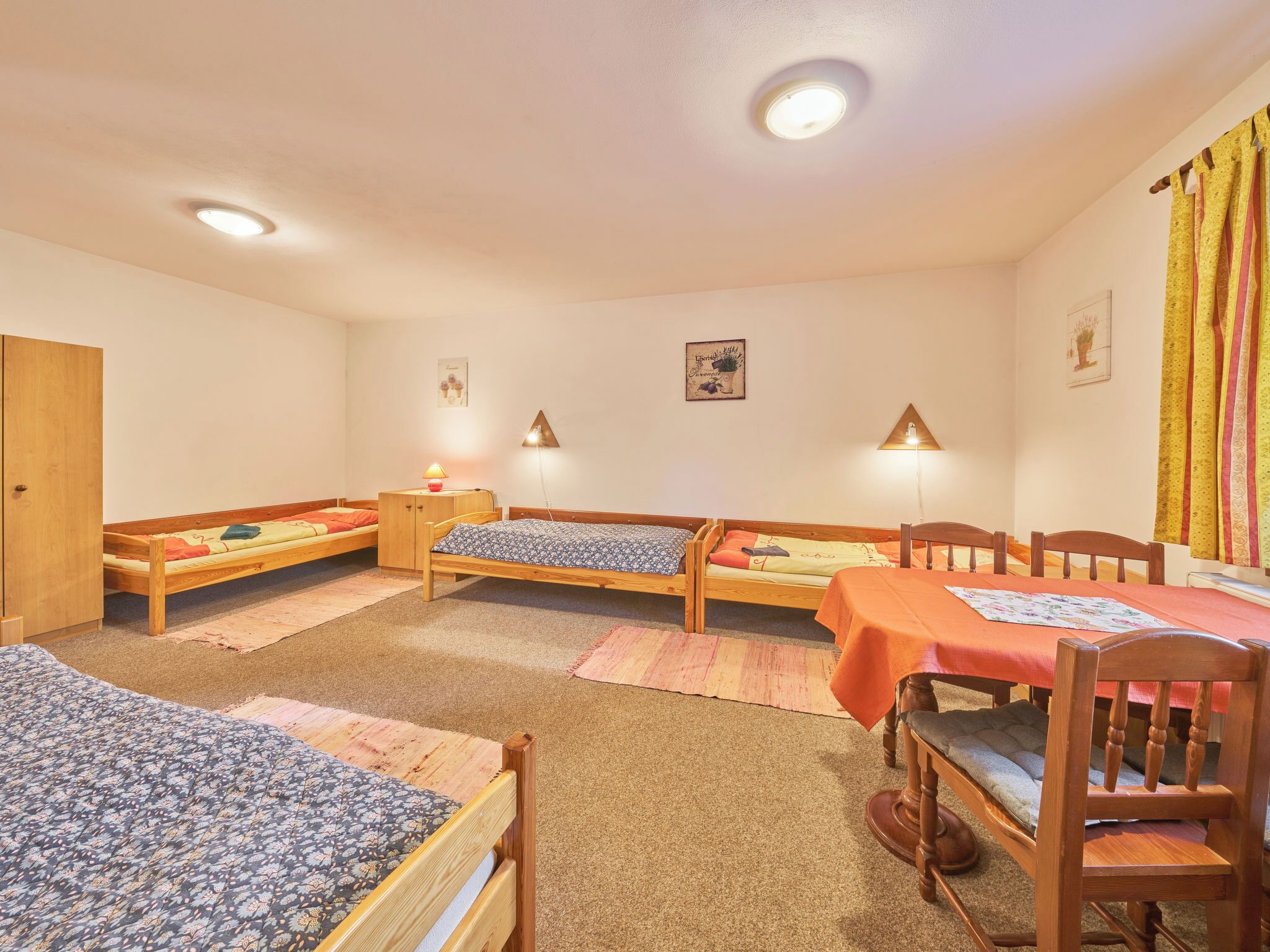 Ein Zimmer mit drei Holzbetten, einem Holztisch mit Stühlen und einem Holzschrank.