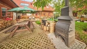 An outdoor patio area with a brick barbecue grill, wooden tables, and a green umbrella.