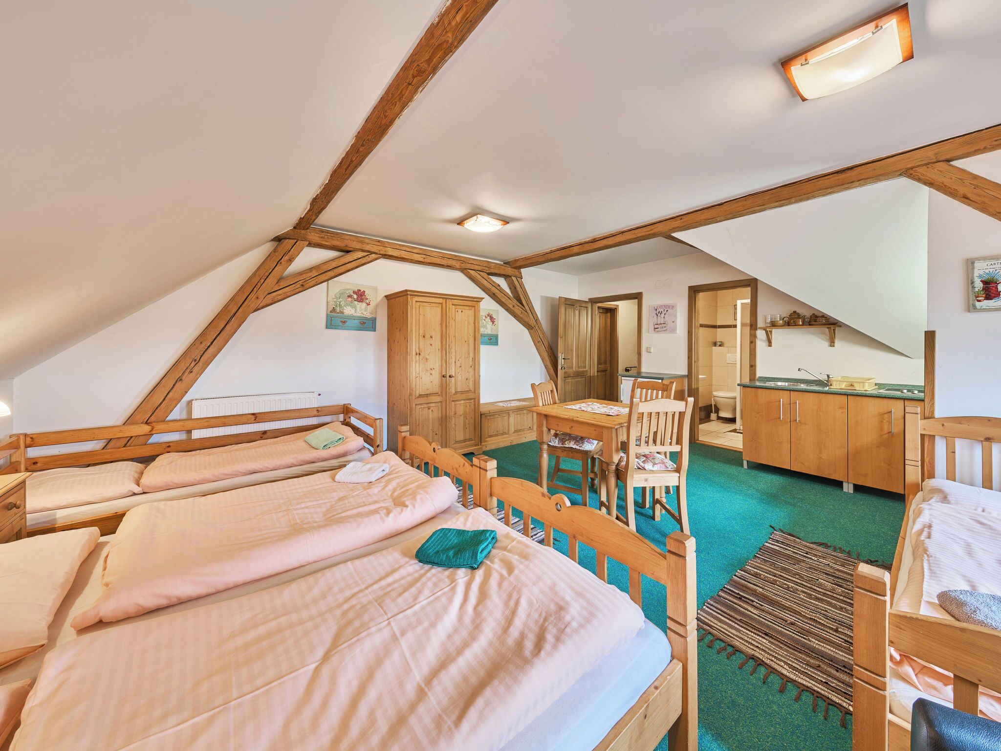 A cozy attic bedroom with wooden beams, a dining table, and a kitchenette.