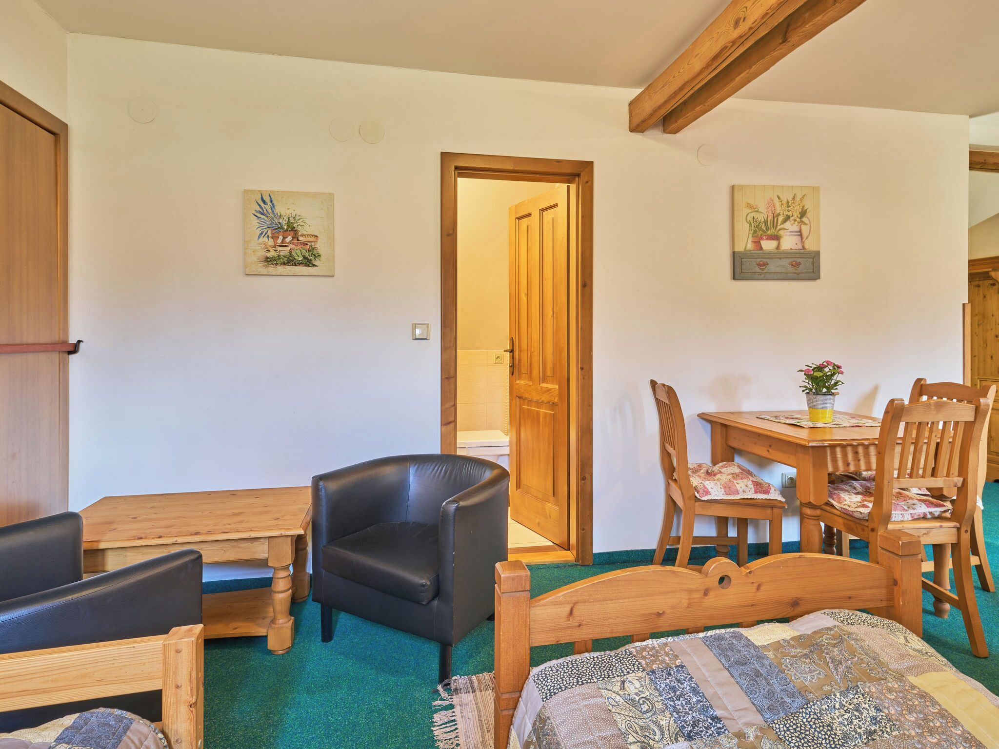 Una habitación acogedora con una cama de madera, un sillón de cuero negro, una mesa de madera con sillas y una puerta que da a otra habitación.