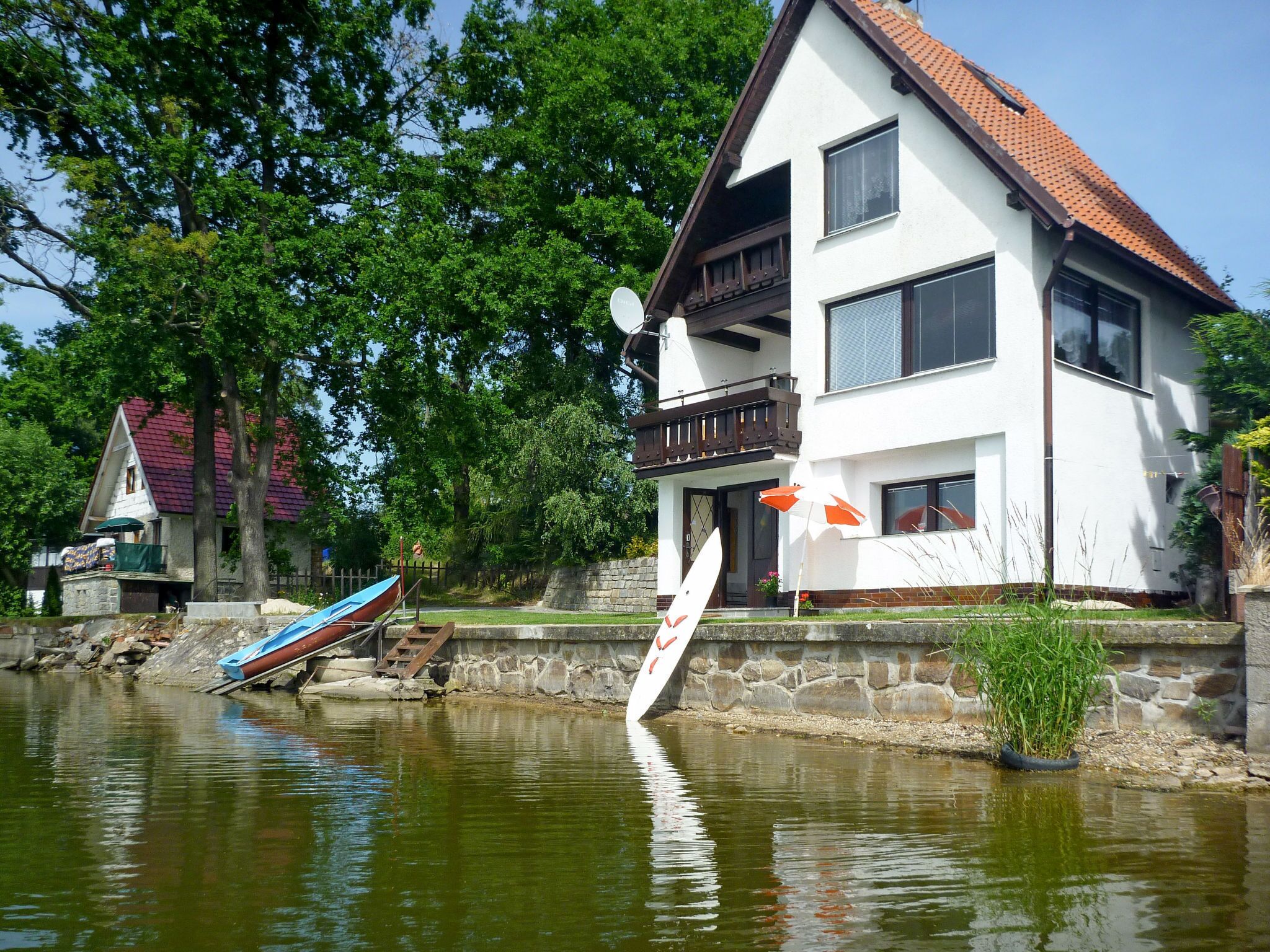 Une maison à deux étages avec un balcon, un petit quai avec un bateau et un mur en pierre.