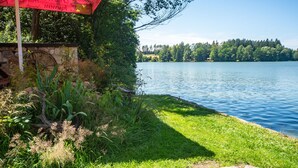 A lakeside view with a grassy area, a stone structure, and a red umbrella. - Lake & Rest by Interhome (Strizovice)
