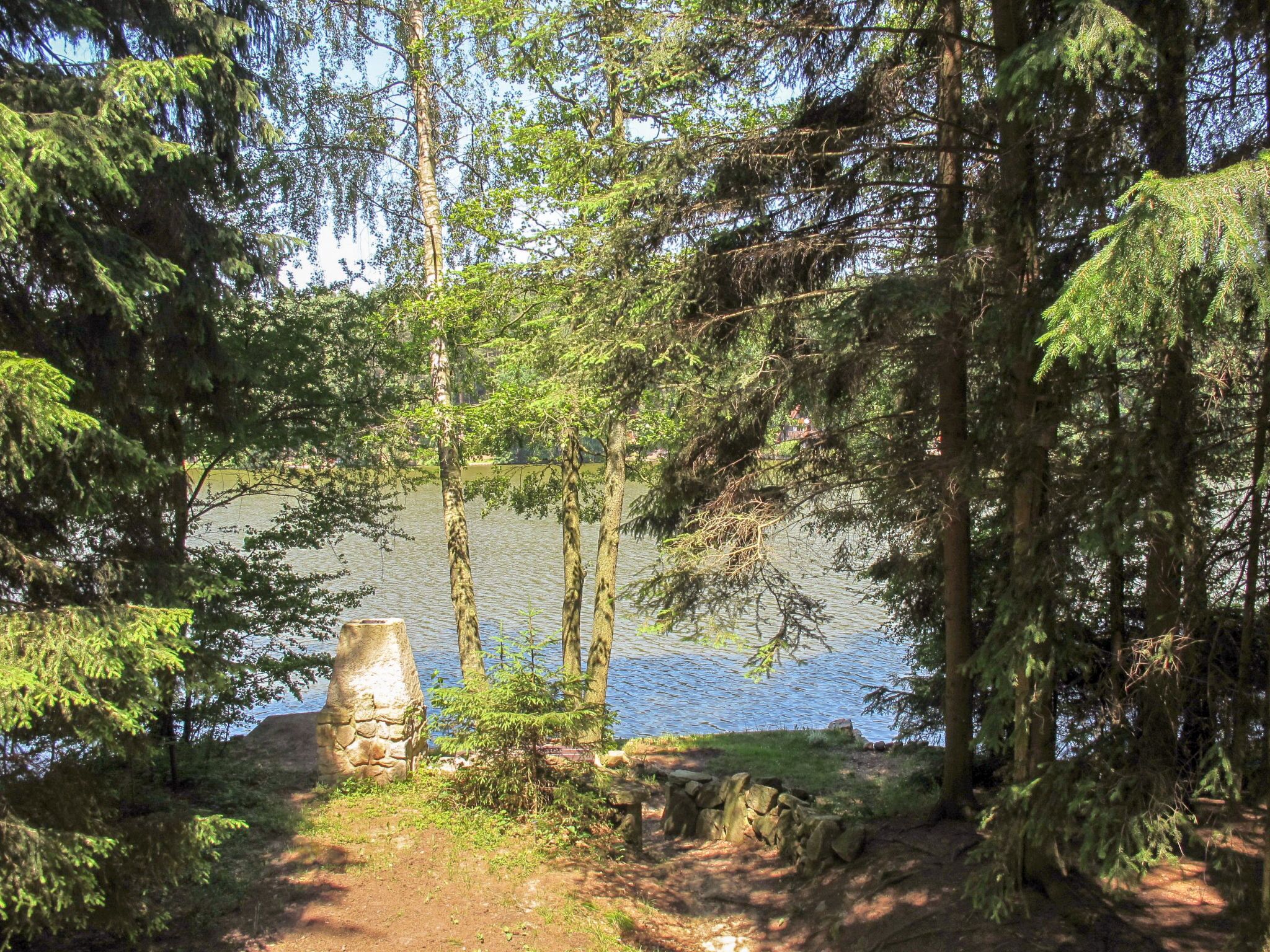 Un área boscosa con un lago, una estructura de piedra y un sendero de tierra.