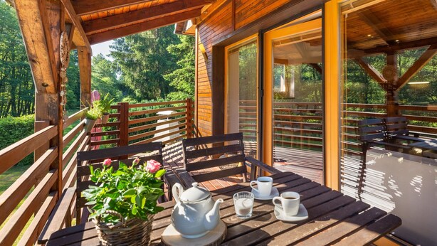 Une terrasse en bois avec une table dressée pour deux personnes, une théière et des tasses.