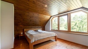 Une chambre avec un plafond en bois, une grande fenêtre et un lit recouvert d’une couverture à carreaux.