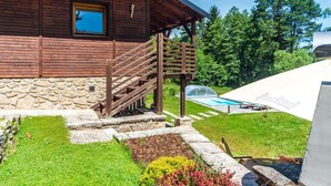 Une cabane en bois avec des fondations en pierre, un escalier en bois, une piscine et un jardin fleuri.