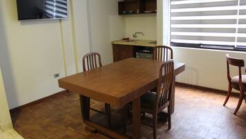 A dining area with a wooden table and chairs, a kitchen with a sink and cabinets, and a window with blinds.