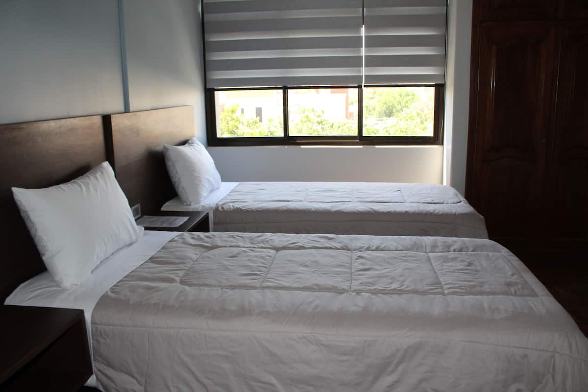 A hotel room with two beds, a window with blinds, and a wooden wardrobe.