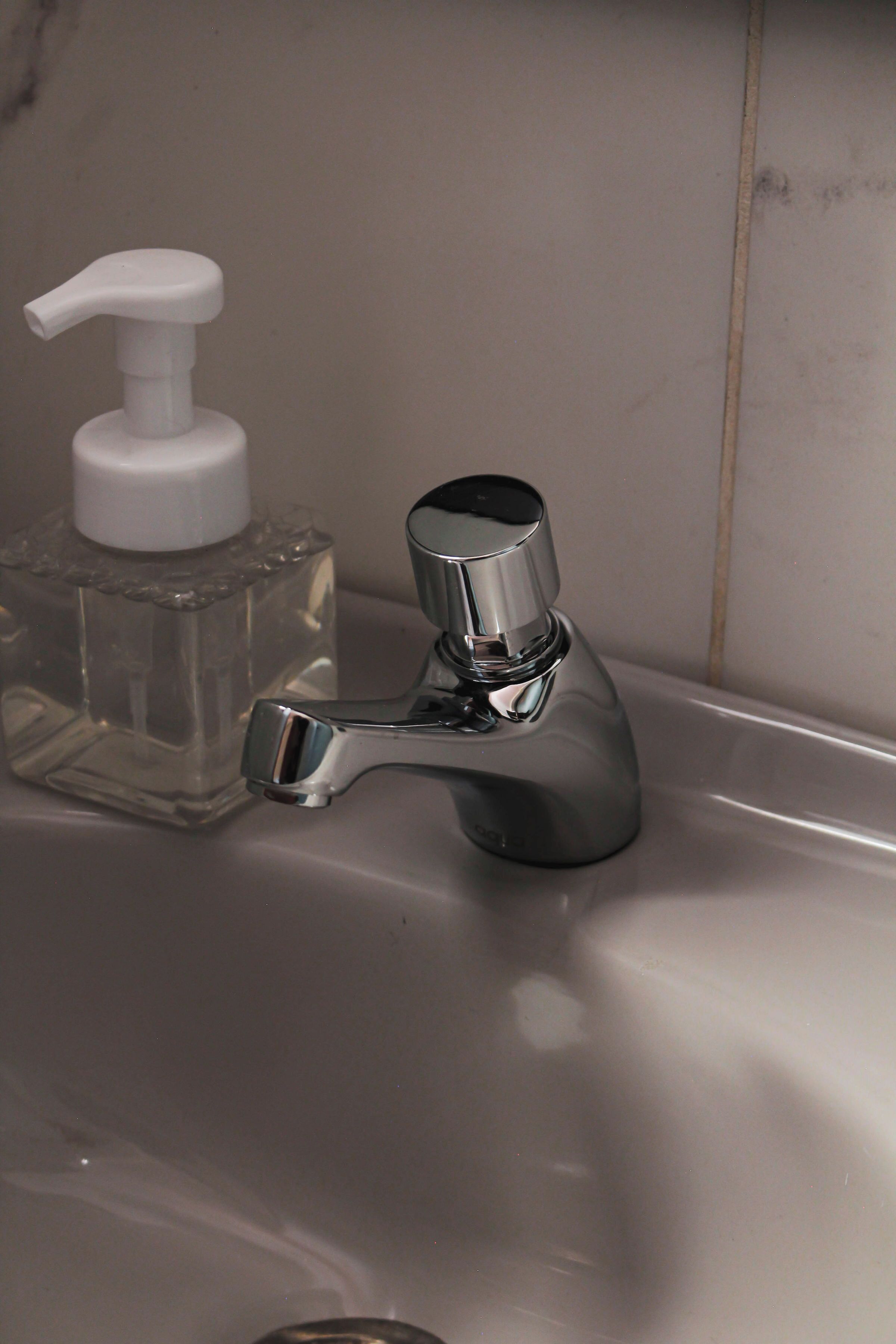 Un lavandino da bagno con rubinetto cromato e dispenser per sapone in vetro trasparente.