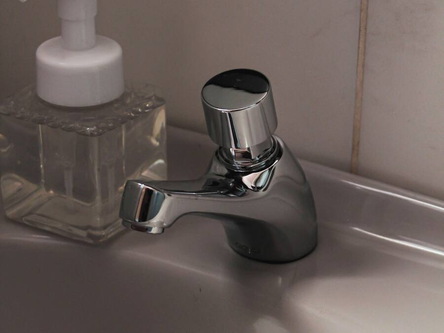 Un lavandino da bagno con rubinetto cromato e dispenser per sapone in vetro trasparente.