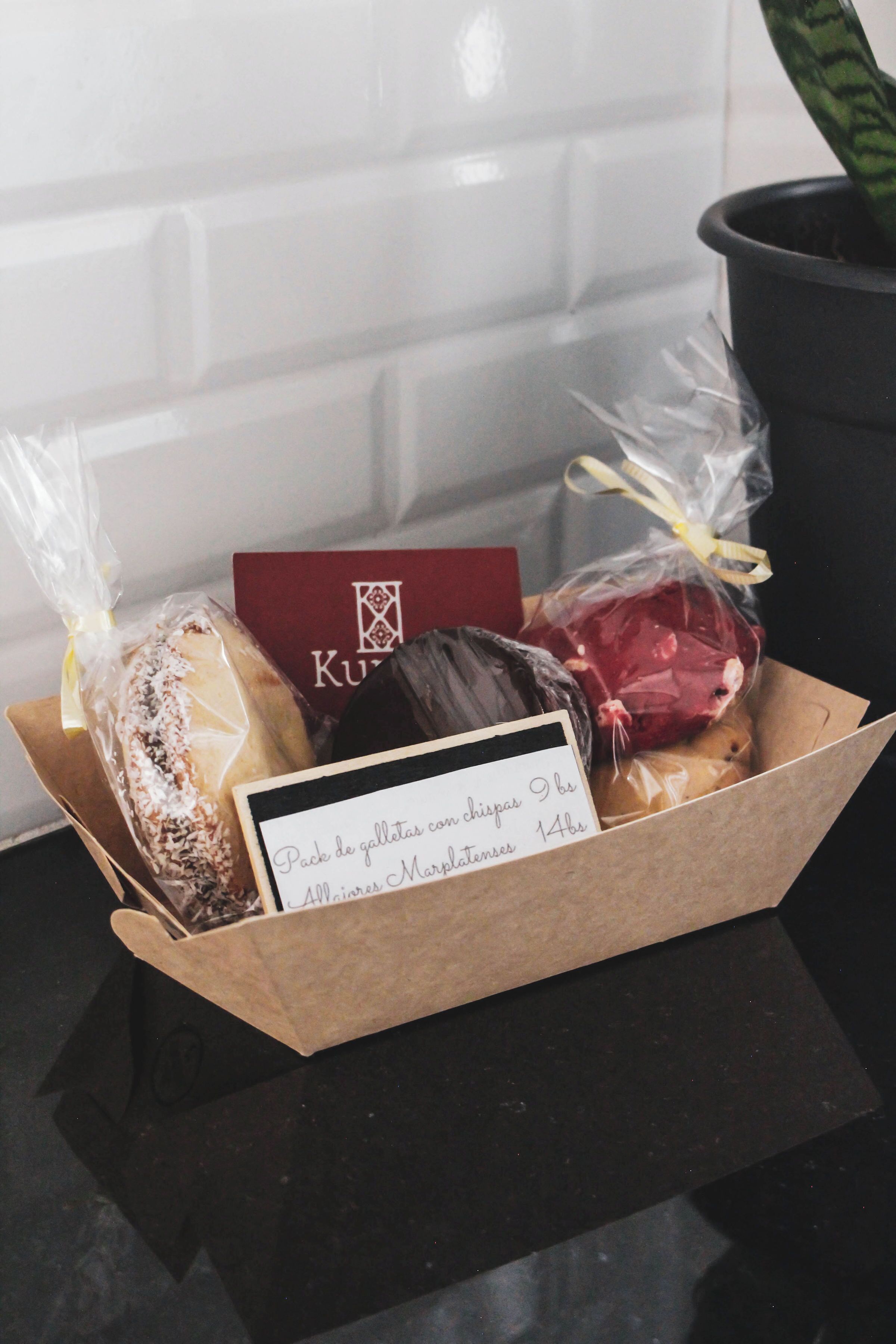 Une boîte cadeau contenant des chocolats et une carte, posée sur une surface sombre, avec une plante en pot en arrière-plan.