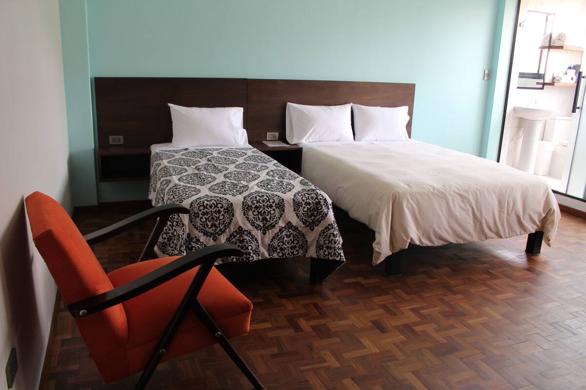 A hotel room with two beds, a wooden floor, and a chair.
