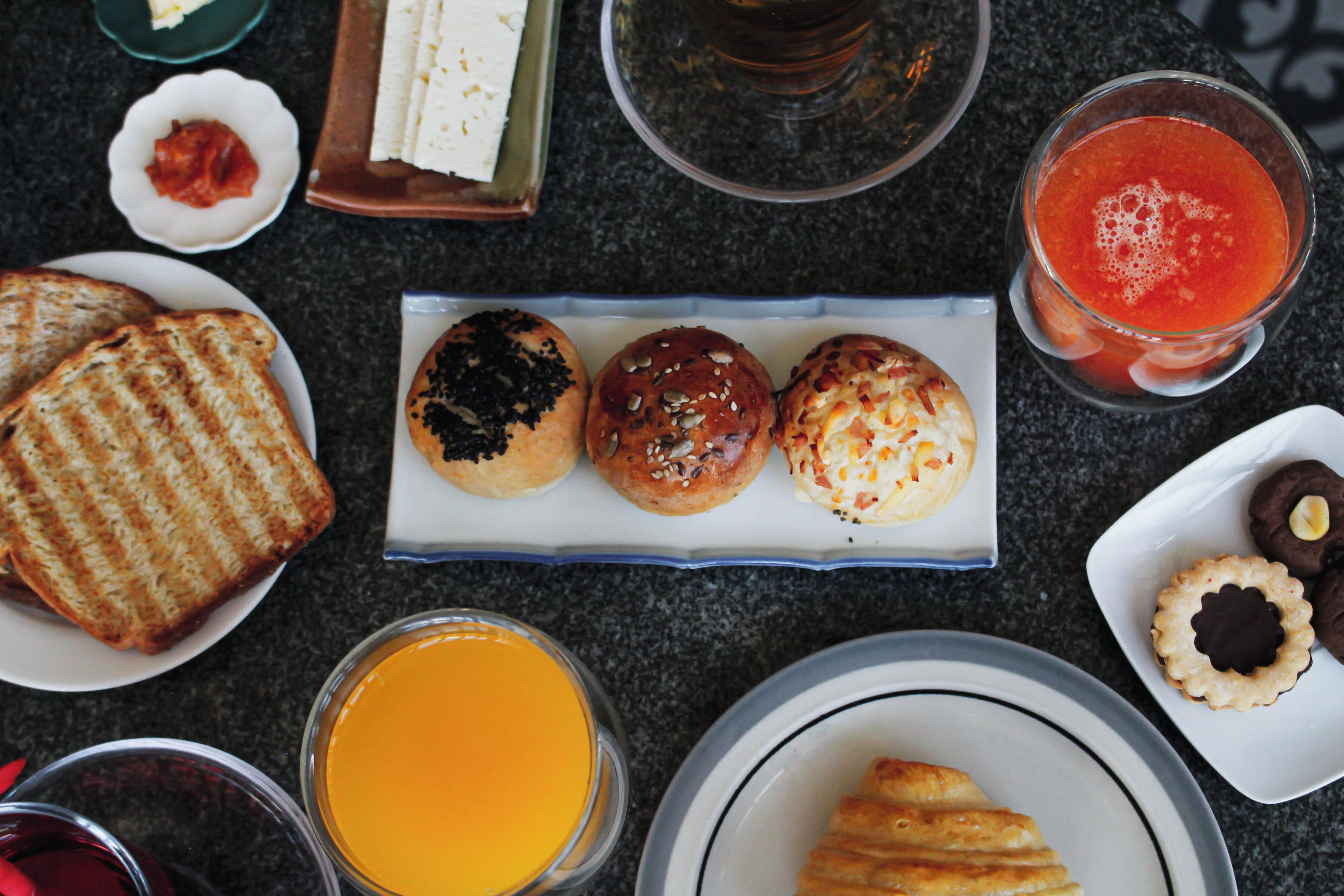 A breakfast table with various food items including toast, muffins, and pastries, along with glasses of juice and coffee.