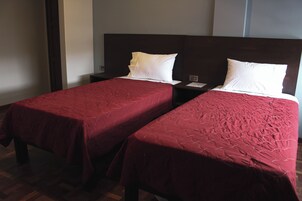 Habitación de hotel con dos camas individuales, cada una con una colcha roja y almohadas blancas.