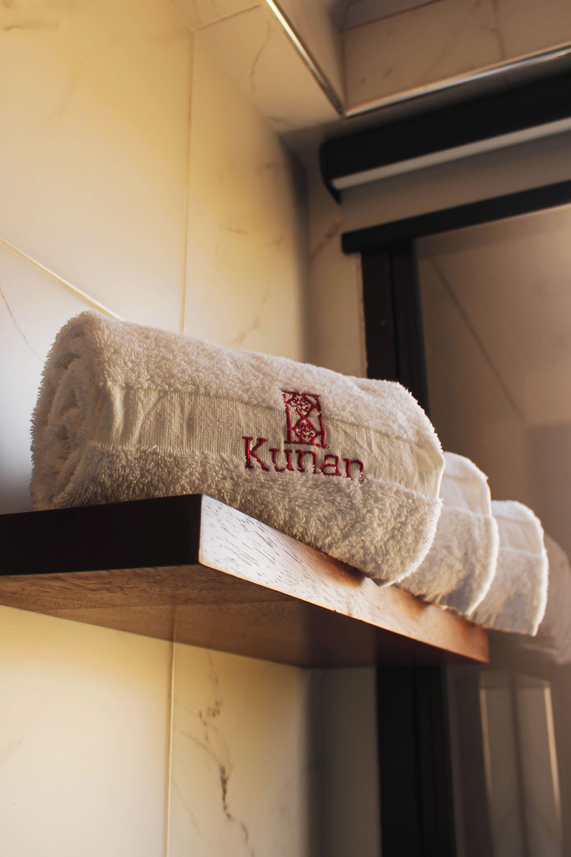 A row of neatly folded towels with embroidered text on a wooden shelf against a tiled wall.