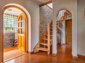 A spacious room with a wooden staircase, a stone wall, and a large wooden door.
