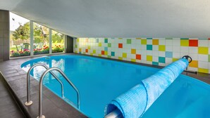 An indoor swimming pool with a tiled wall, a metal pool ladder, and a view of a garden through large windows. - Haus Polivka by Interhome (Hurka u Nemcice)