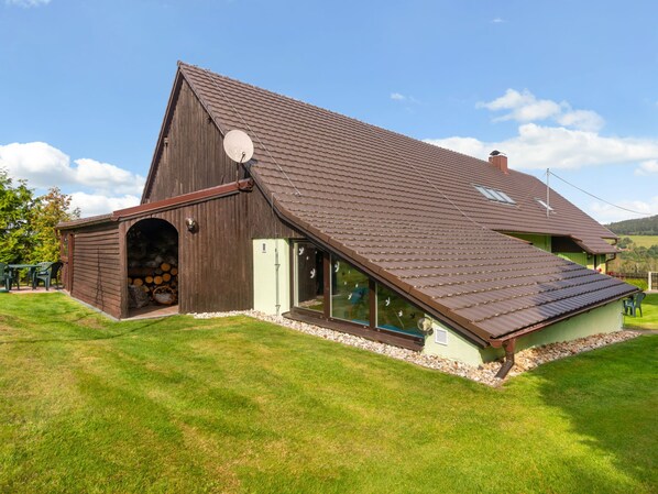 A large barn with a sloped roof, a satellite dish, and a door leading to a covered area with logs.