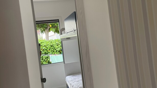 Un corridoio stretto che porta a una camera da letto con un letto, una piccola finestra e vista sul verde.