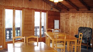 A wooden dining room with a large table and chairs, a patterned armchair, and a window with a view of trees. - Chalet Anthamatten by Interhome (Champery)