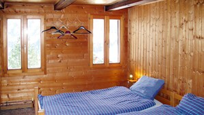 A wooden cabin room with two beds, a wooden ceiling, and a window with a view of trees. - Chalet Anthamatten by Interhome (Champery)