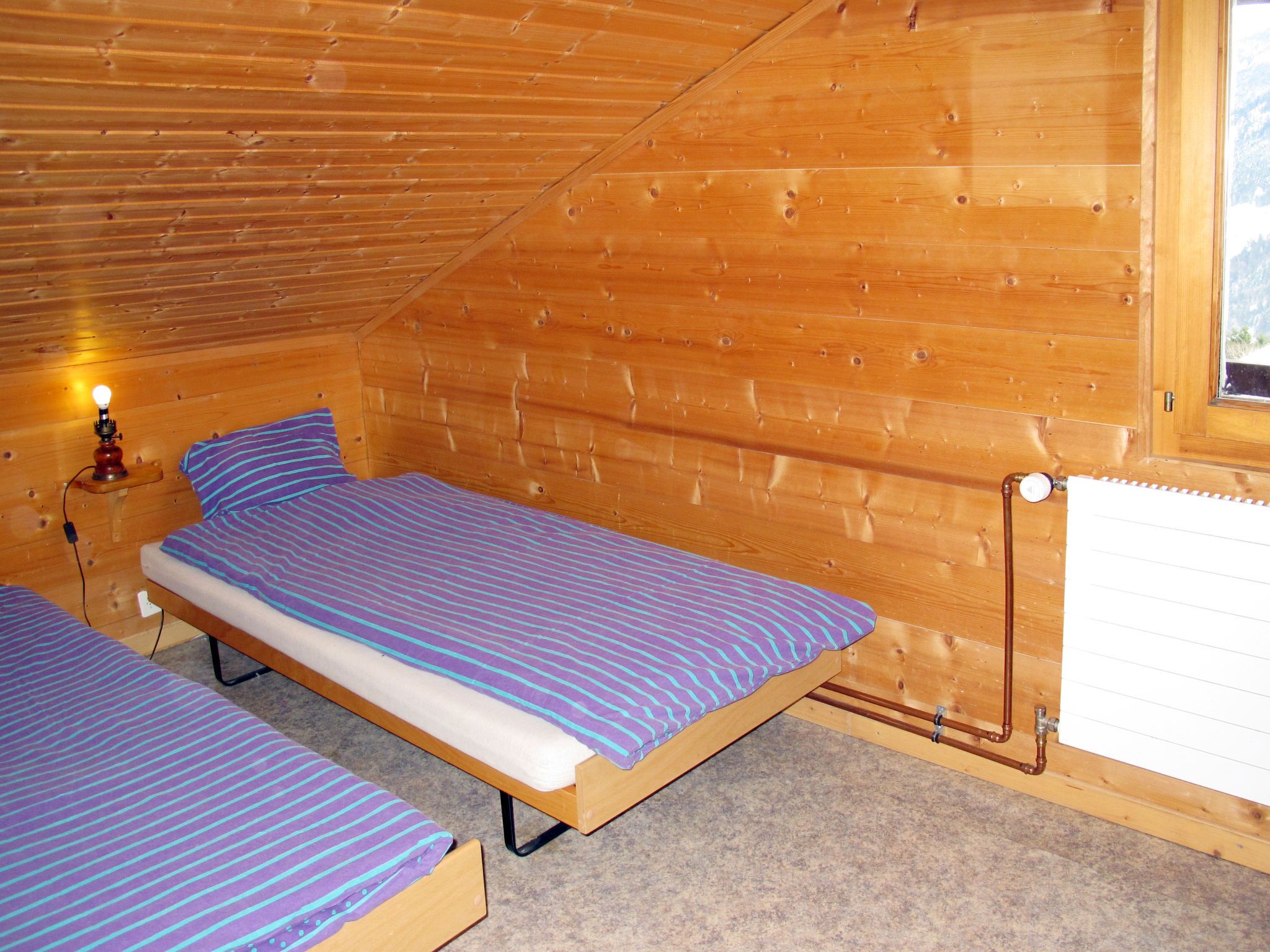 Una pequeña habitación tipo cabaña de madera con dos camas, una mesita de noche y una ventana.