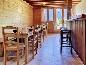 Interior em madeira com uma longa mesa de jantar, cadeiras e um espaço de bar.