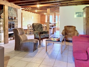 A cozy living room with a stone fireplace, wooden beams, and a tiled floor.