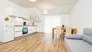 Une cuisine moderne avec des meubles blancs, un four encastré et un coin repas comprenant une table et des chaises en bois.