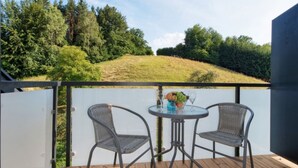 Un balcon avec deux fauteuils en osier et une petite table ronde, donnant sur une colline verdoyante et une forêt dense.
