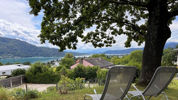 Two outdoor lounge chairs with a lake and mountains in the background. - Apartment Meran by Interhome (Pörtschach am Wörthersee)