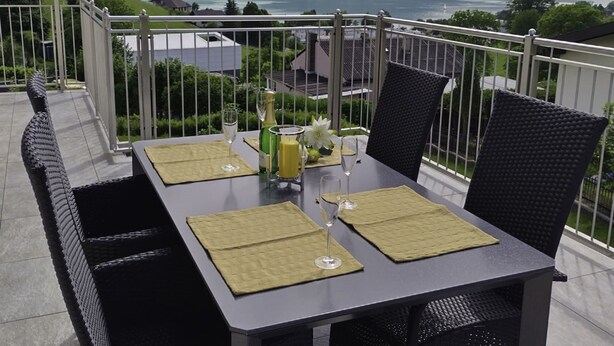 A balcony with a table set for two, overlooking a scenic view of a lake and mountains. - Apartment Meran by Interhome (Pörtschach am Wörthersee)