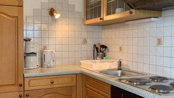 Een koelkast, een oven, kookgerei, borden en bestek, eettafels