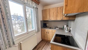 A compact kitchen with wooden cabinets, a built-in stove, and a window with patterned curtains. - Landhaus Grüne Oase by Interhome (Öblarn)