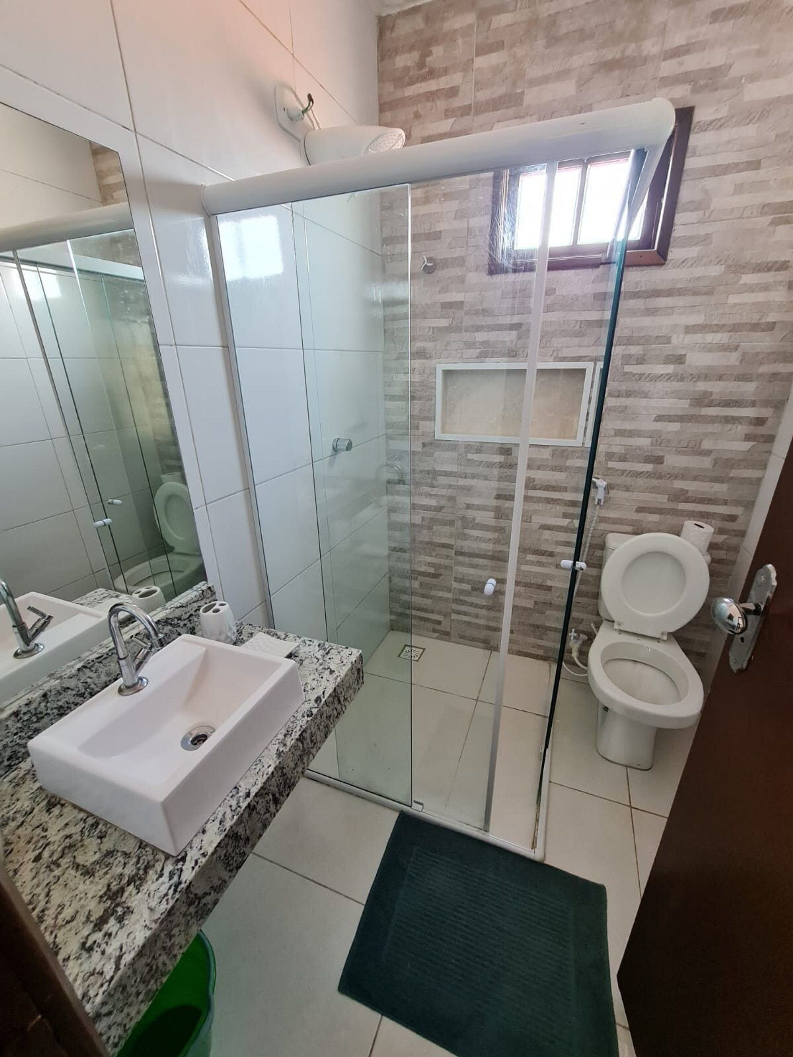 A modern bathroom with a glass shower enclosure, a sink with a granite countertop, and a toilet.