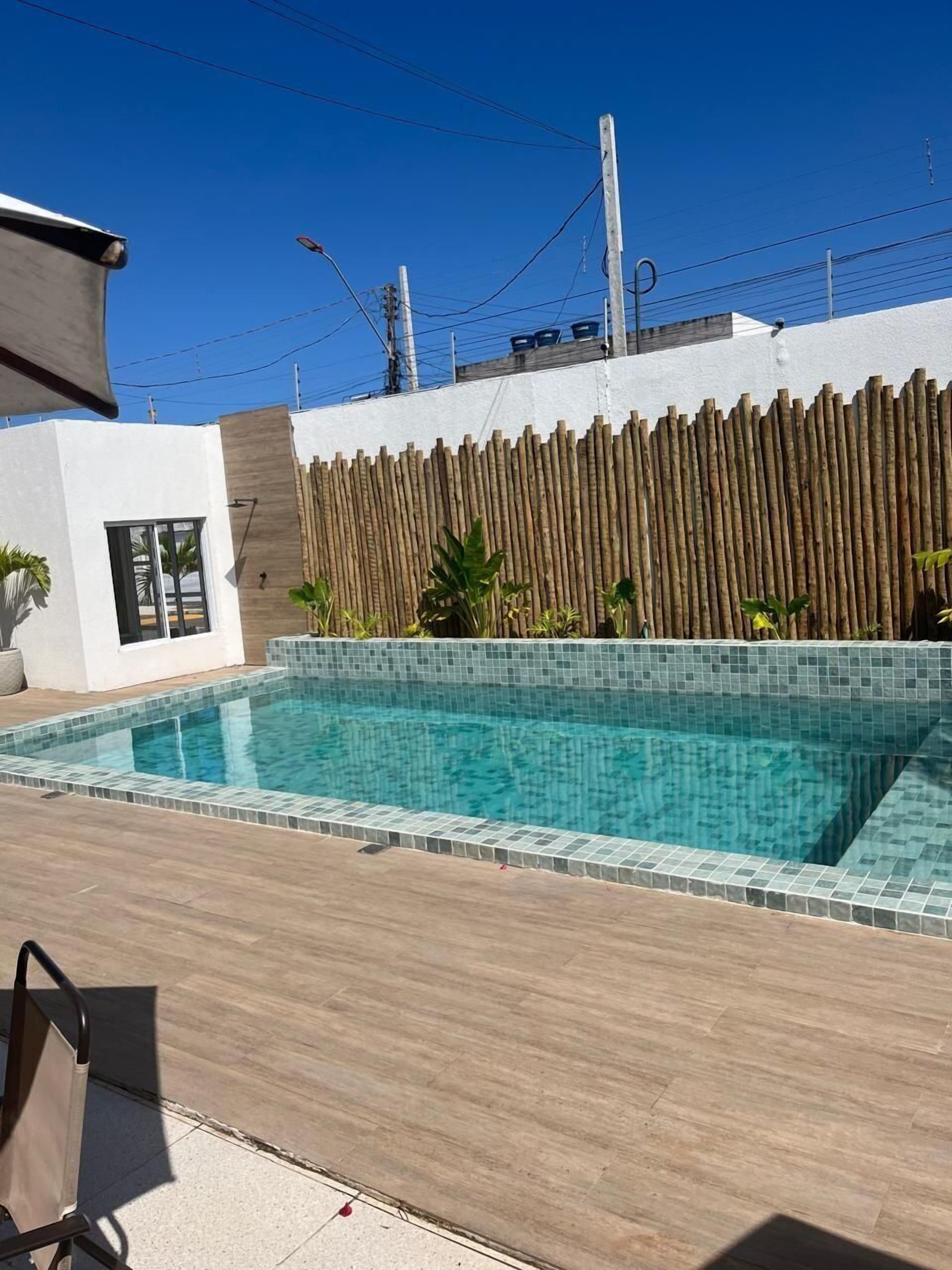 A modern outdoor swimming pool with a tiled edge, surrounded by a wooden fence and a white wall.