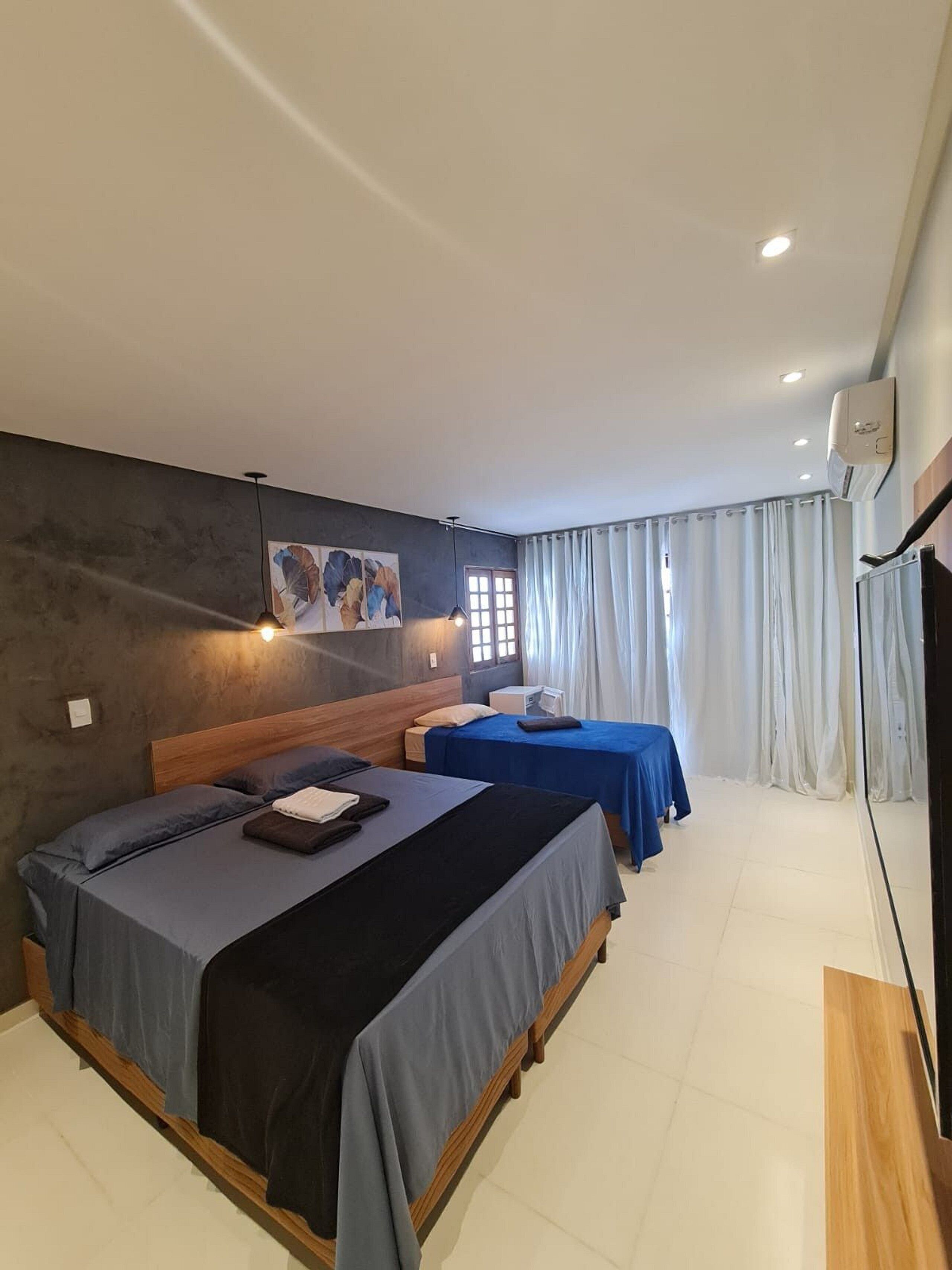 A hotel room with two beds, a painting on the wall, a window with curtains, and a ceiling fan.